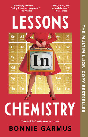 A white woman shown from the shoulders down, wearing a red knee-length dress and red shoes stands in front of a periodic table in gold on a red background. She is carrying a portable tube-style TV.  The word "in" from the title is superimposed on the TV screen in black block letters.  The words "LESSONS"  and "CHEMISTRY" from the title are imposed on the red background in white, all caps font.