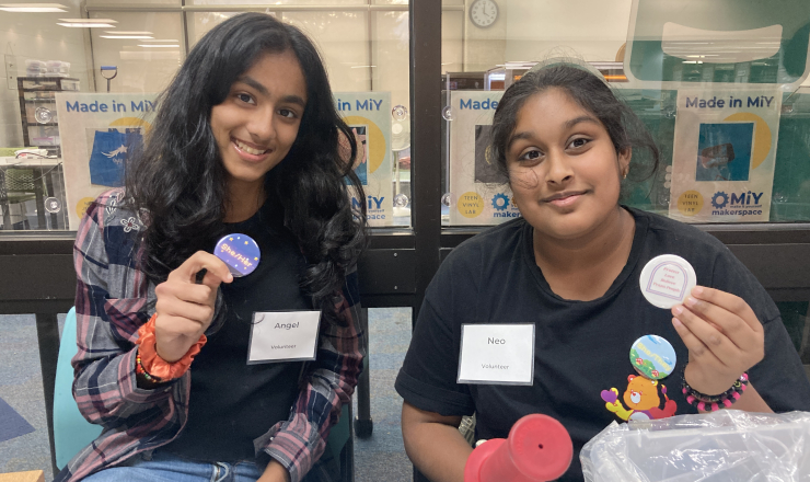 Two teens with button maker outside of makerspace